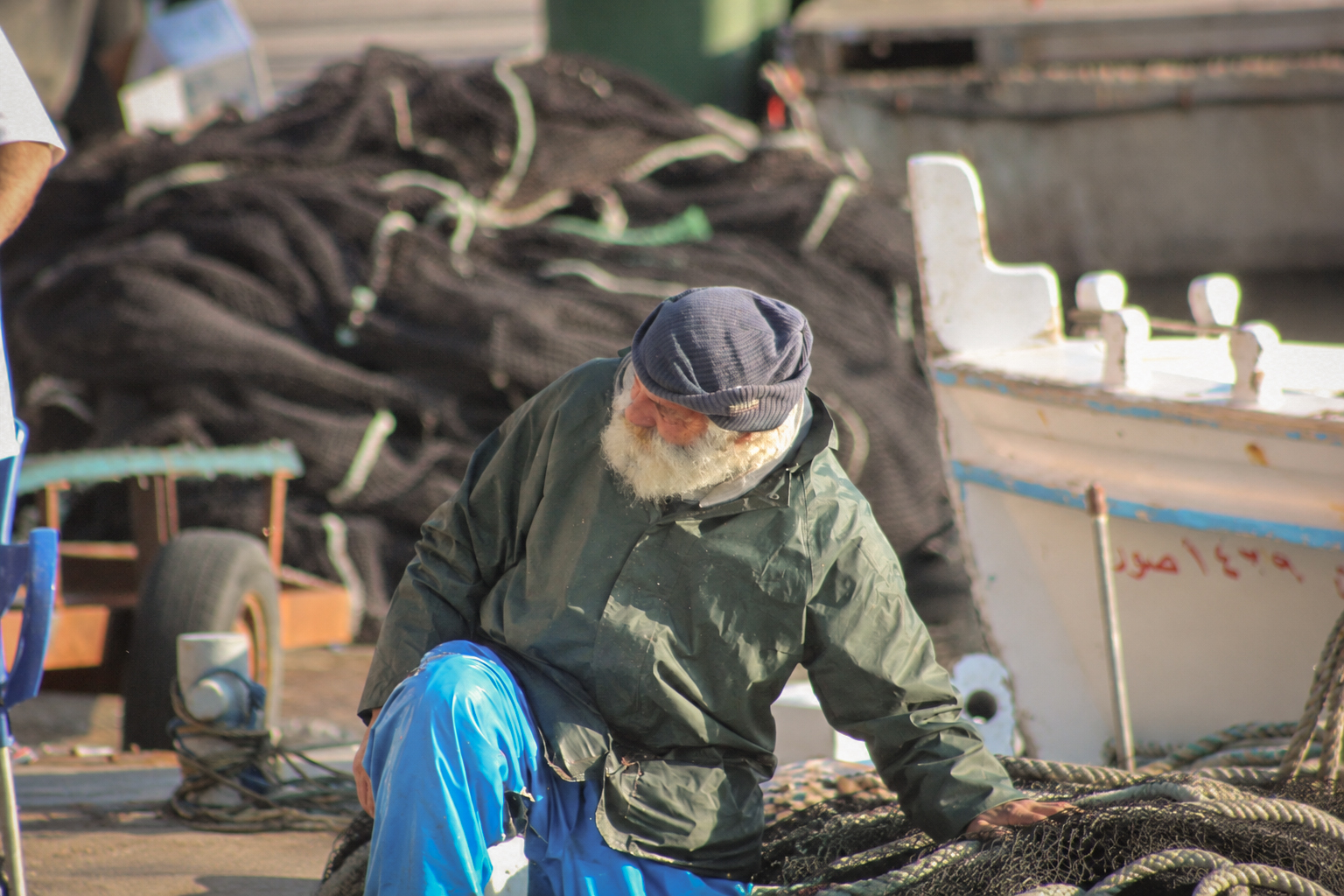 Un pêcheur en casquette qui trie ses filets près des barques