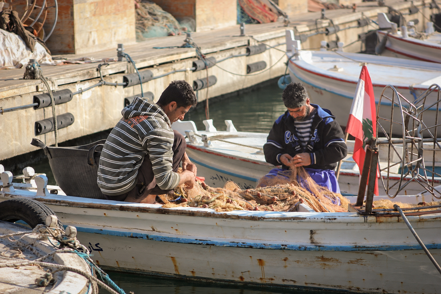 Deux pêcheurs au travail dans une barque sous le drapeau libanais